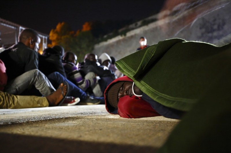 An ill irregular immigrant lies on the ground as a blanket is placed over him at the Armed Forces of Malta (AFM) Maritime Squadron base at Haywharf in Valletta's Marsamxett Harbour, early June 8, 2014.  129 Sub-Saharan African migrants were rescued by the AFM south of the Maltese islands when their boat ran into difficulties, according to army sources.