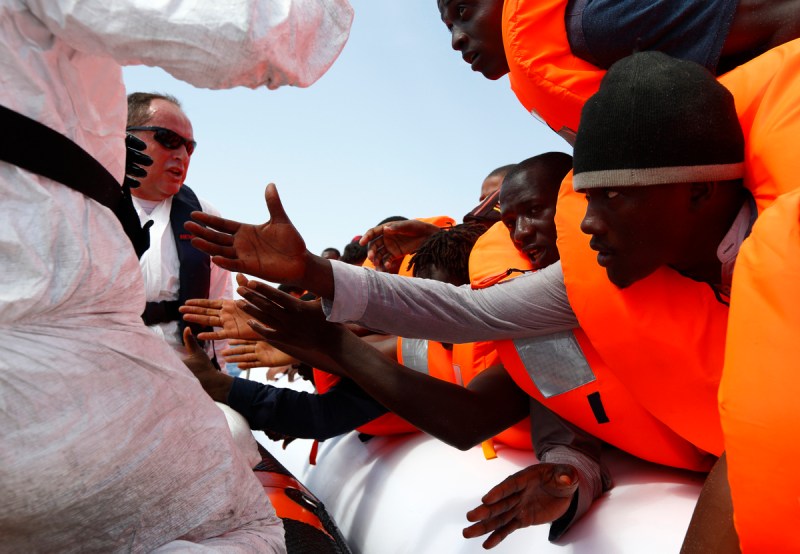 Migrants reach out to grab hold of Migrant Offshore Aid Station  rescuers on a RHIB before  being taken to the MOAS ship MV Phoenix some 20 miles off the coast of Libya